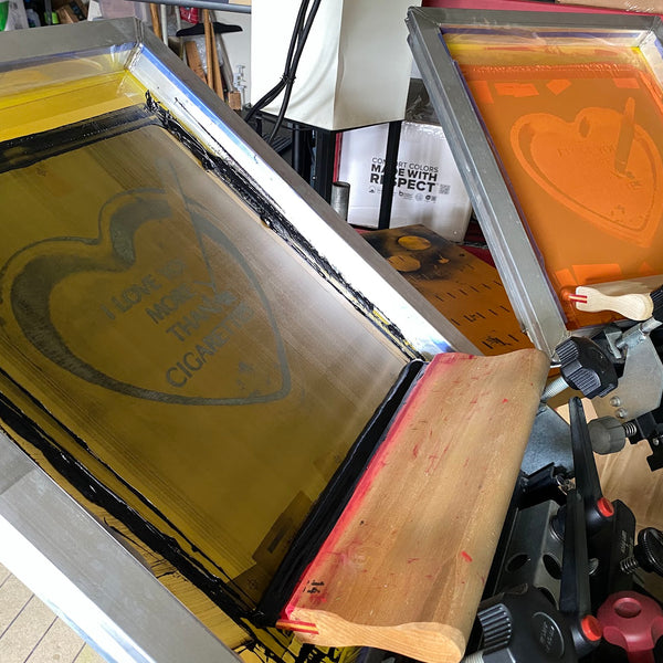 I Love You More Than Cigarettes heart screen coated in yellow ink with the squeegee at RVA Threads screen printing, Virginia