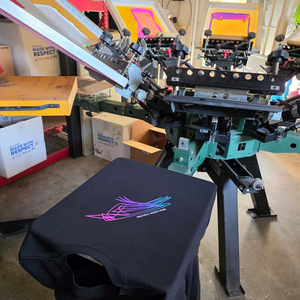 Iron Crow Theatre print on a black tee in front of the press with blue, purple and pink screens at RVA Threads screen printing, Virginia