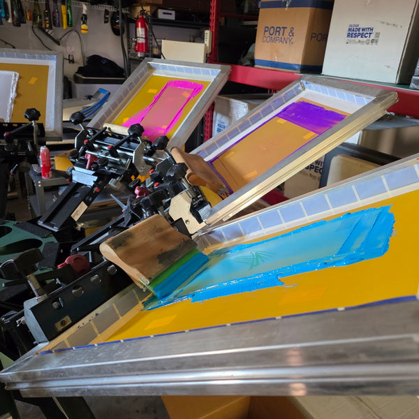Iron Crow Theatre screens loaded with blue, purple and pink ink on the press at RVA Threads screen printing, Virginia