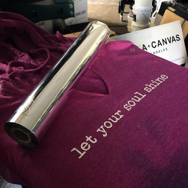 Let Your Soul Shine lettering in silver foil on a maroon tee beside the foil roll at RVA Threads screen printing, Virginia