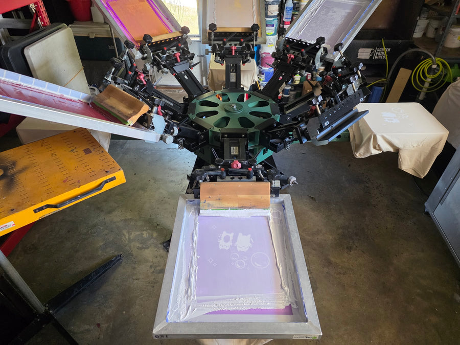 Manual press loaded with purple emulsion screens and wood squeegees, a cream tee on one platen at RVA Threads screen printing, Virginia