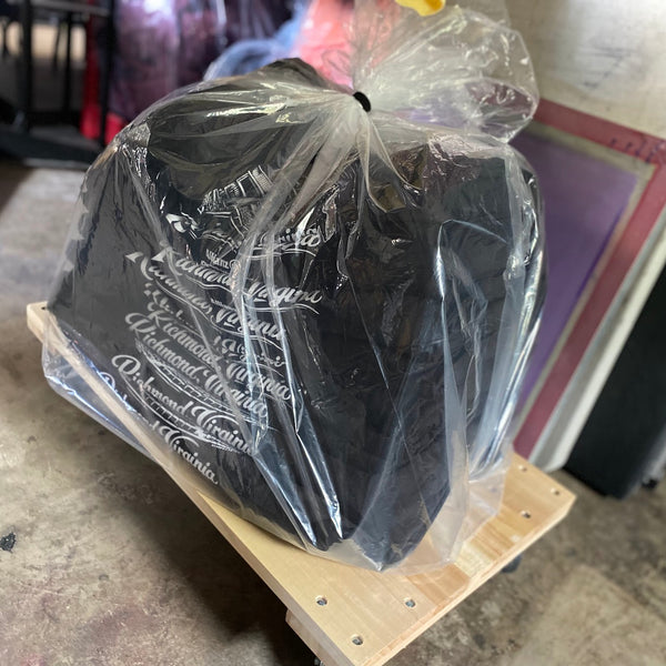 Printed black tees bagged in clear plastic on a pallet, ready for delivery at RVA Threads screen printing, Virginia