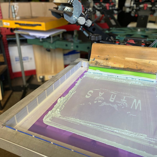 Screen flooded with white ink and the squeegee resting on the press, ready for a pull at RVA Threads screen printing, Virginia