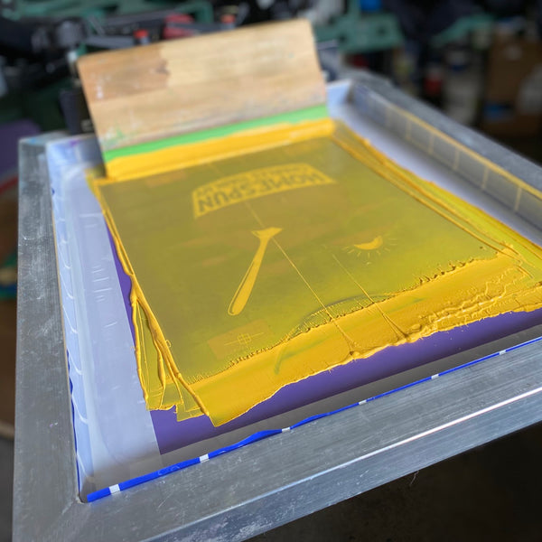 Screen flooded with yellow ink and a squeegee resting on the press, ready to pull at RVA Threads screen printing, Virginia