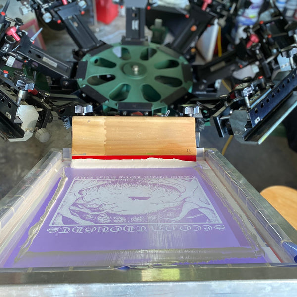 Screen with red ink and a squeegee on the press for a circular eye graphic at RVA Threads screen printing, Virginia