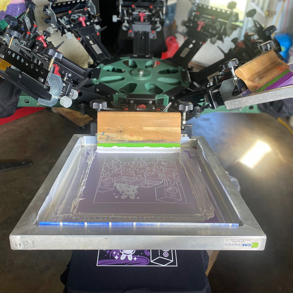Screen with white ink and the squeegee on the press over a printed black tee at RVA Threads screen printing, Virginia