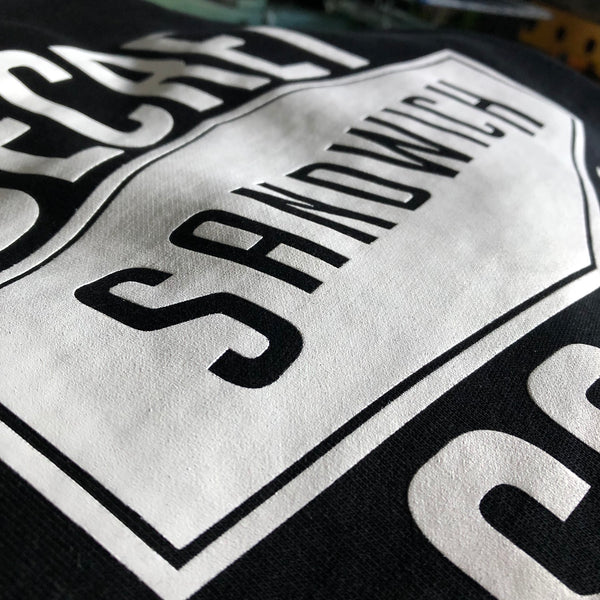 Secret Sandwich Society sandwich sign design in white ink on a black tee, close up at RVA Threads screen printing, Virginia