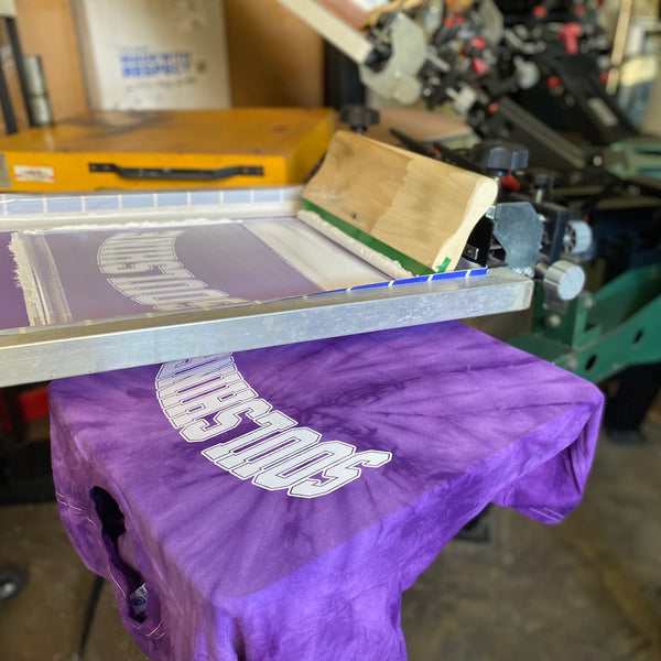 Soulshine purple tie-dye tee on the press under the raised screen at RVA Threads screen printing, Virginia