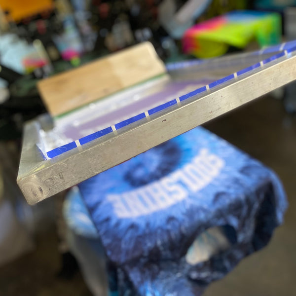 Soulshine arch lettering screen raised over a freshly printed blue tie-dye tee on the press at RVA Threads screen printing, Virginia