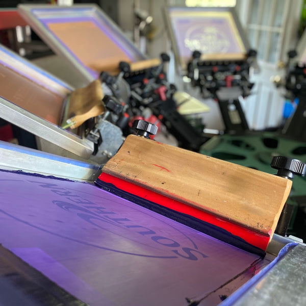 Southern Sweep logo screen with the squeegee resting on the press between prints at RVA Threads screen printing, Virginia