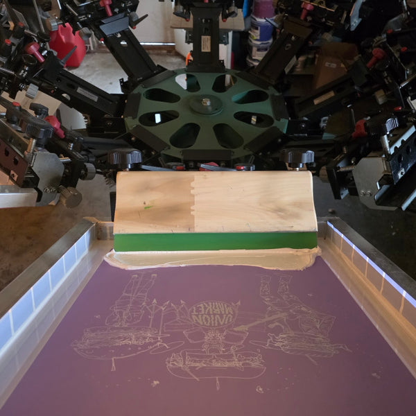 Union Market sandwich band screen with white ink and the squeegee on the six-color press at RVA Threads screen printing, Virginia