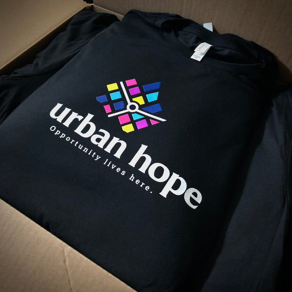 Urban Hope Opportunity Lives Here logo in full color on a black tee, boxed at RVA Threads screen printing, Virginia