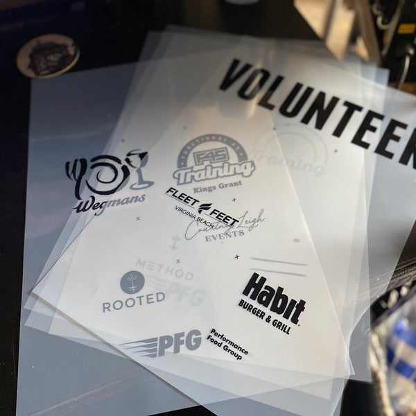 Volunteer back print film positives with sponsor logos laid out on the press at RVA Threads screen printing, Virginia