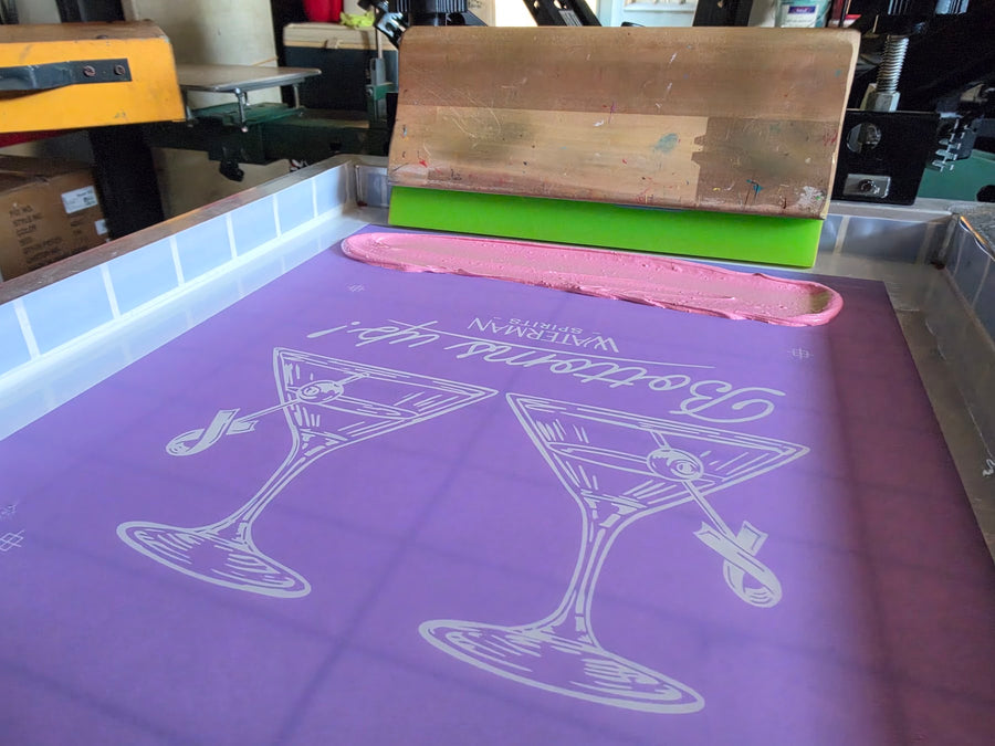 Waterman Spirits Bottoms Up screen with a bead of pink ink and a wood squeegee on the press at RVA Threads screen printing, Virginia