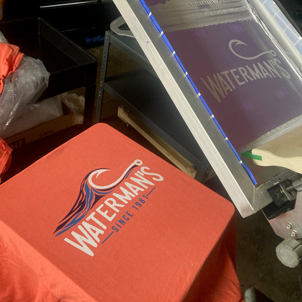 Waterman's wave logo on a coral tee with the screen on the press at RVA Threads screen printing, Virginia