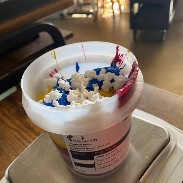 Cup of white, blue, yellow and red ink on a digital scale while mixing a custom color at RVA Threads screen printing, Virginia