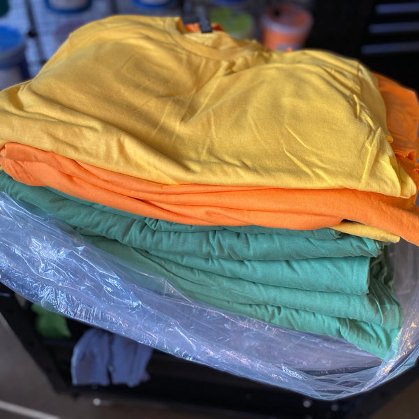 Stack of yellow, orange and green tees folded on a plastic bag at RVA Threads screen printing, Virginia