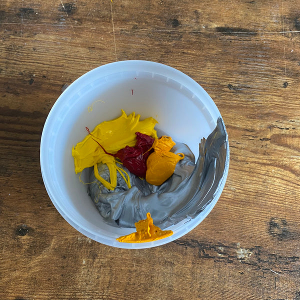 Cup of yellow, red, orange and gray ink being mixed for a custom color on the bench at RVA Threads screen printing, Virginia